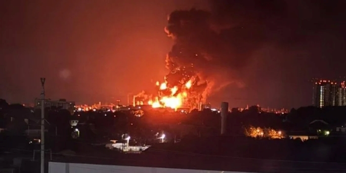 Massive fire and explosion at night, with thick black smoke rising over an industrial area on the Russian oil refinery, illuminating the surrounding city buildings.