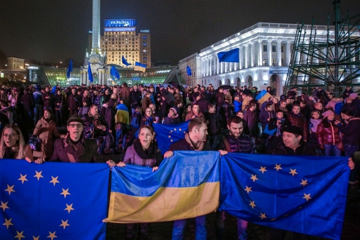 A large crowd gathers on Kyiv’s Independence Square (Maidan Nezalezhnosti) at night, holding EU and Ukrainian flags in support of European integration. The illuminated cityscape and flags symbolize Ukraine’s pro-European movement and solidarity with the European Union.
