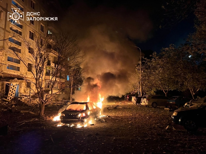 At night in Zaporizhzhia, Ukraine, a car burns near a damaged residential building after a Russian missile strike.