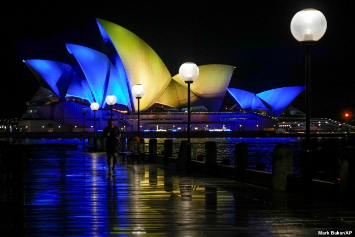 The Sydney Opera House illuminated in blue and yellow lights at night, reflecting over the wet waterfront in Sydney, Australia. The iconic landmark shines brightly, symbolizing solidarity with Ukraine