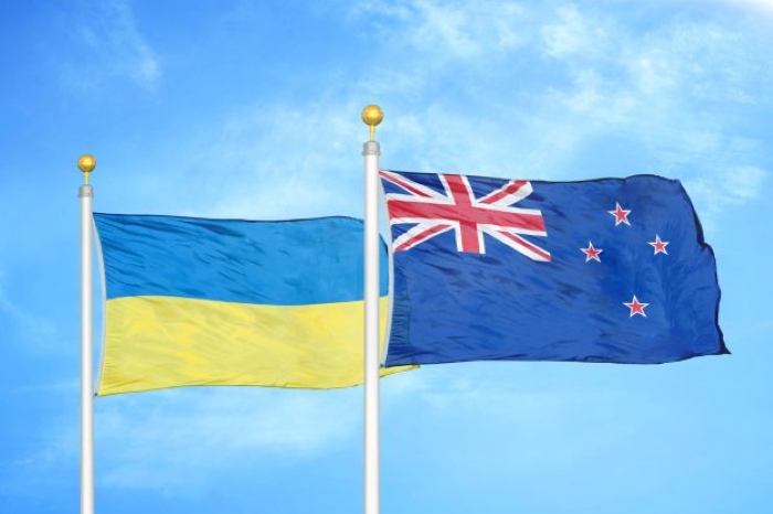 National flags of Ukraine and New Zealand waving side by side against a bright blue sky, symbolizing friendship, diplomatic relations, and international cooperation between the two countries.