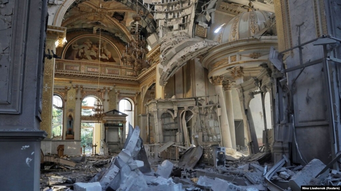 The image shows the heavily damaged interior of the Transfiguration Cathedral in Odesa, Ukraine, after a Russian missile strike. Debris covers the floor, and the once-grand baroque and neoclassical architecture lies partially destroyed, with shattered columns, fallen chandeliers, and frescoes visible amid the ruins — a powerful symbol of Russia’s attacks on Ukraine’s cultural heritage