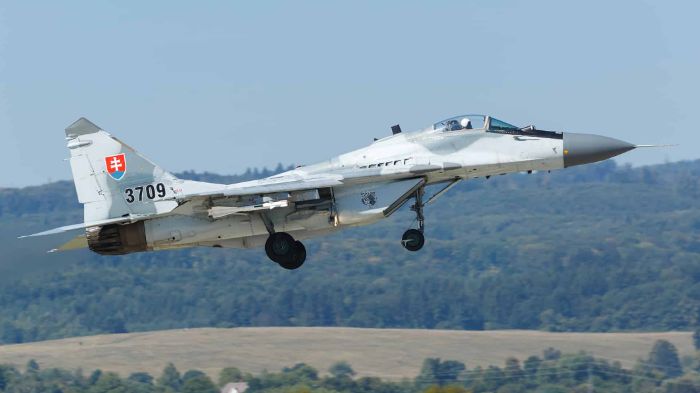 Slovak Air Force MiG-29 fighter jet taking off with landing gear extended against a mountainous landscape. T