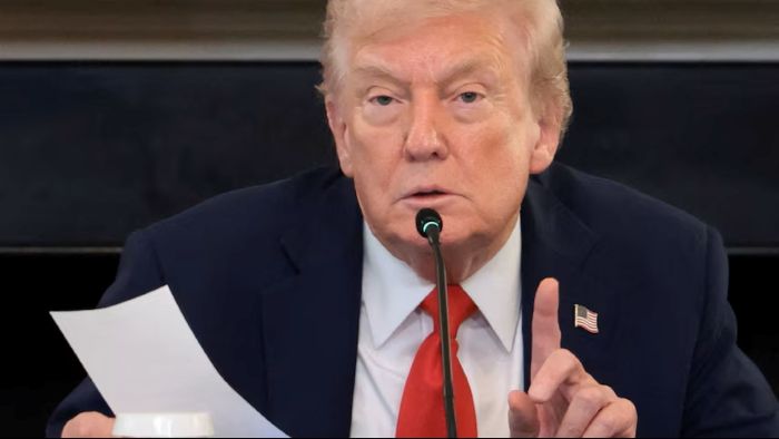 U.S. President Donald Trump speaks into a microphone while holding a sheet of paper during a formal meeting.