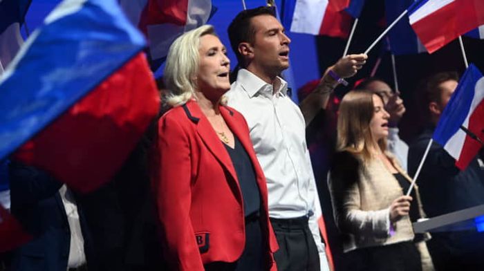 French National Rally right-wing party leaders Marine Le Pen and Jordan Bardella are standing surrounded by French flags