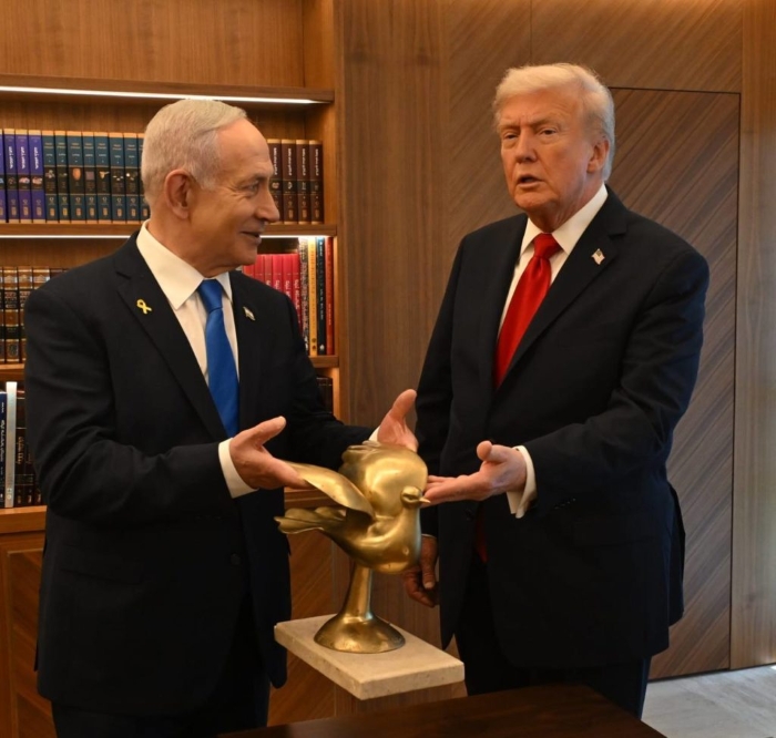 U.S. President Donald Trump and Israeli Prime Minister Benjamin Netanyahu are seen standing together in an office, discussing a golden dove statue symbolizing peace. The image captures Trump in a red tie and dark suit, while Netanyahu wears a blue tie, both appearing engaged in a diplomatic conversation surrounded by wooden bookshelves — symbolizing U.S.-Israel relations and recent peace efforts.