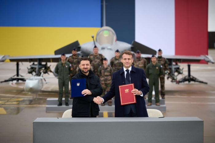 Volodymyr Zelenskyy and Emmanuel Macron are pictured shaking hands after signing a document on the background of flags and Rafale jet