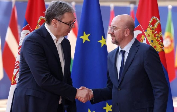 Serbian President Aleksandar Vučić and former President of European Council Charles Michel are depicted shaking haands an flags background
