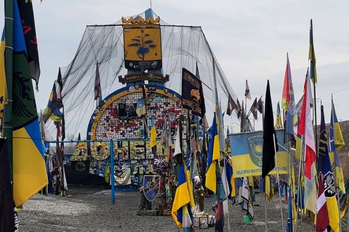 A powerful memorial installation at the entrance to Donetsk Region, covered with Ukrainian flags, military insignias, and tribute messages.