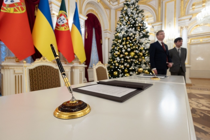 A ceremonial signing table with a pen in the foreground during an official meeting between Ukraine and Portugal, with Ukrainian and Portuguese flags displayed behind