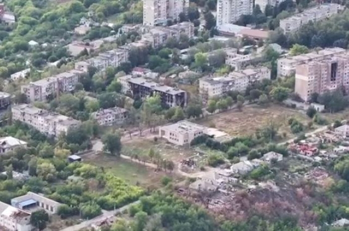 Aerial view of a residential district in Kypiansk showing multi-story apartment buildings surrounded by greenery, with visible damage and debris in part of the area