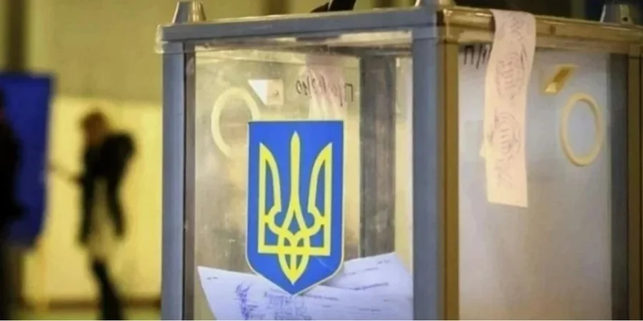 A transparent Ukrainian election ballot box with the national coat of arms (the Tryzub) stands in a polling station, filled with voting papers. In the background, a voter is seen near a voting booth.