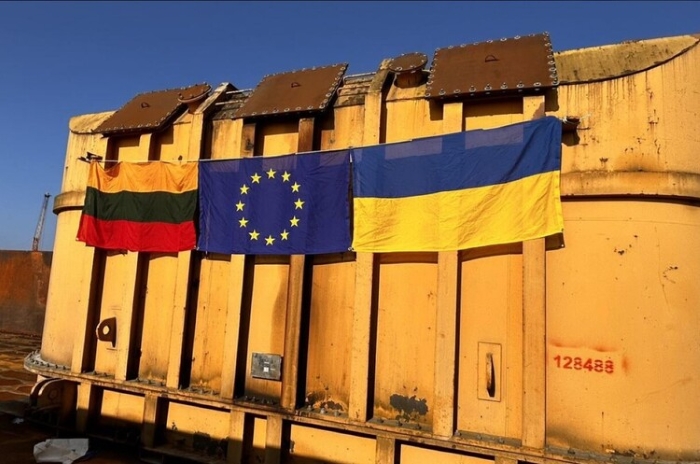 The image shows heavy container with three flags hanging on it: Lithuania, the European Union, and Ukraine.