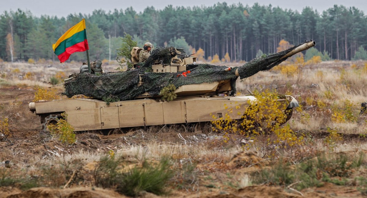 The photo shows a battle tank during training or testing at a training ground, with the Lithuanian flag flying above it.