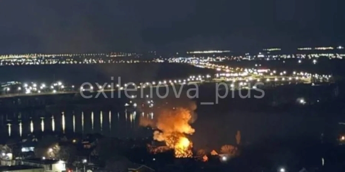 A nighttime aerial view shows a large fire burning near a waterfront industrial area in Rostov, with bright flames and thick smoke rising from the site of an apparent strike.