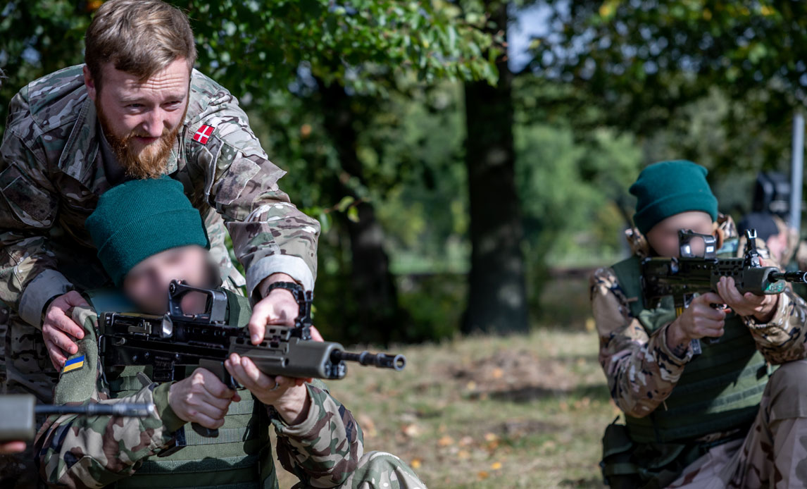 The picture shows a Danish soldier teaches Ukrainian recruits basic weapons handling
