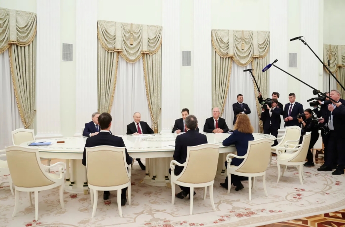 A high-level diplomatic meeting between Russian President Vladimir Putin, Presidential Representative Kirill Dmitriev, and Foreign Policy Advisor Yuri Ushakov, US President Donald Trump's Special Representative Steve Witkoff and son-in-law Jared Kushner takes place in an ornate government hall with a long white oval table