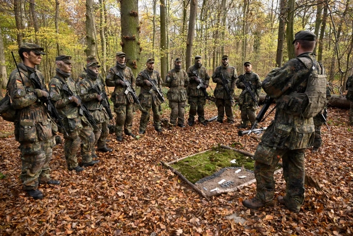 A group of European soldiers in camouflage undergo tactical training during exercises in a forest area. Soldiers with small arms stand in a semicircle around their commander, who explains the task at hand.A group of European soldiers in camouflage undergo tactical training during exercises in a forest area. Soldiers with small arms stand in a semicircle around their commander, who explains the task at hand.