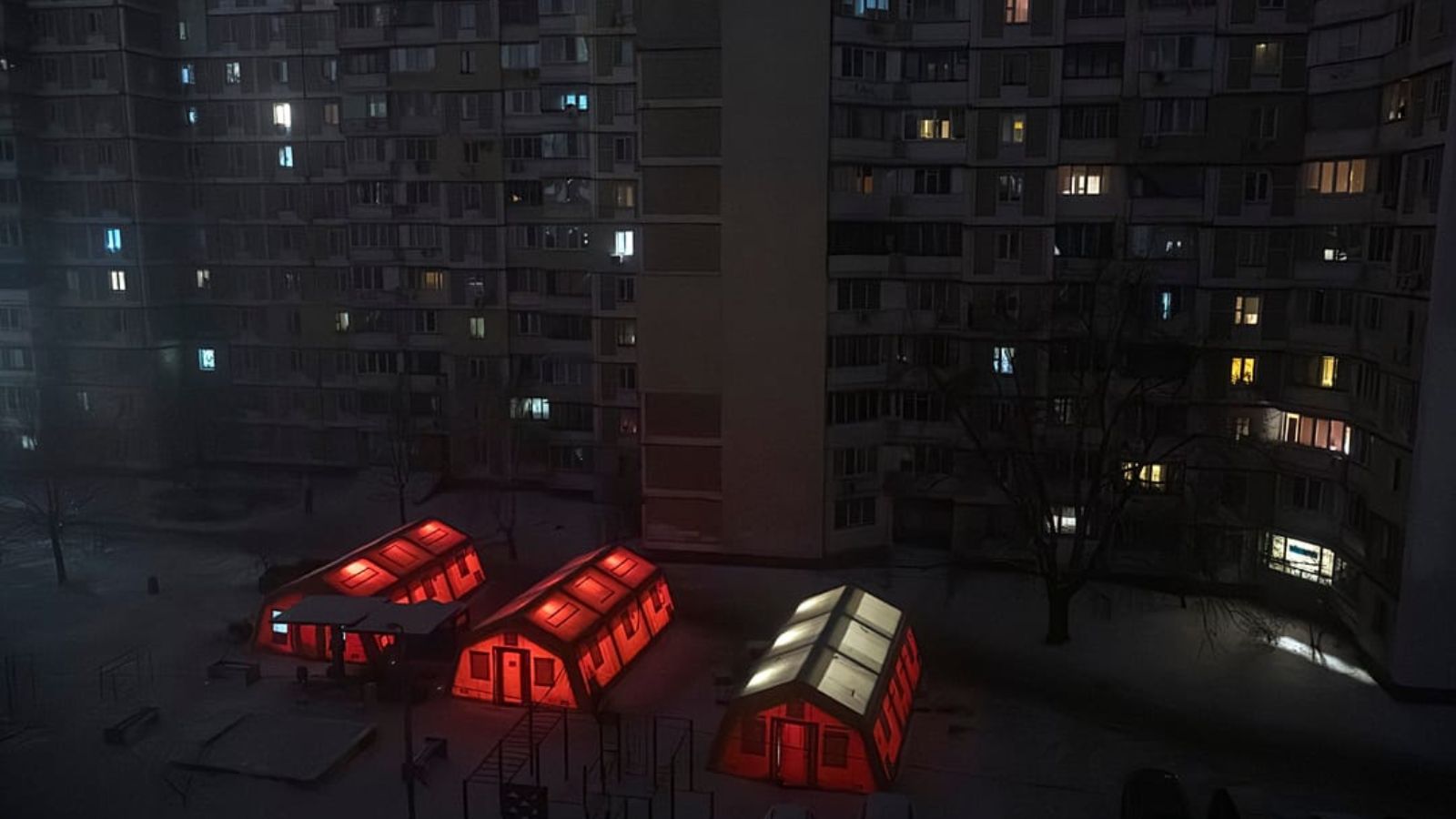 Three illuminated emergency heating tents glowing orange and yellow in a dark courtyard of high-rise apartment buildings during a blackout in Kyiv.