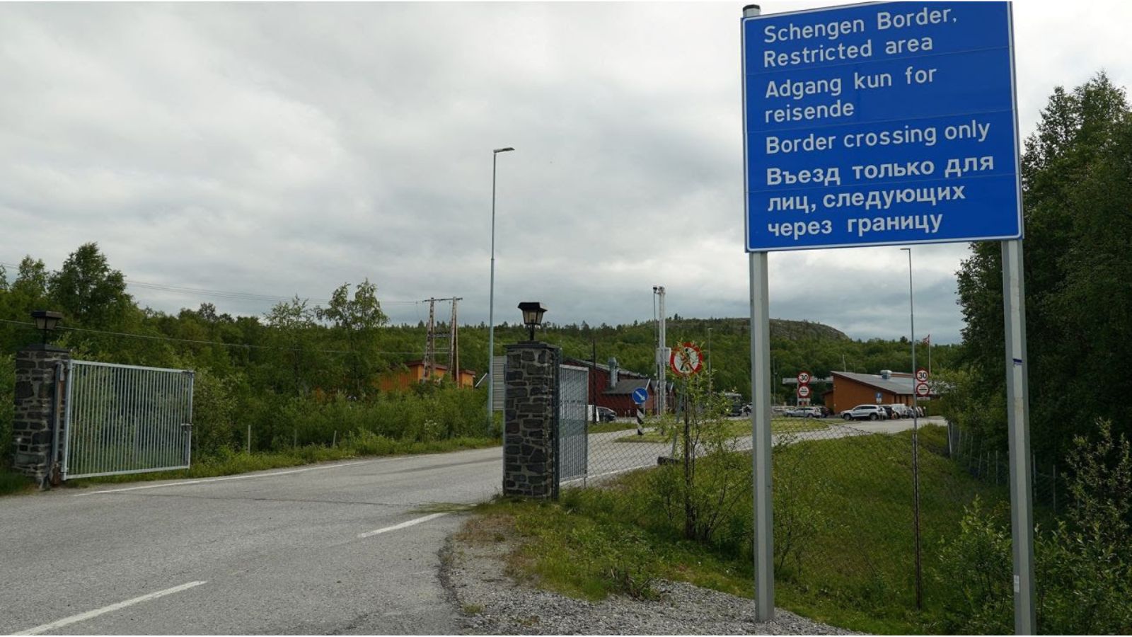 A blue road sign marking the Schengen Border and restricted area at the crossing between Norway and Russia, with text in English, Norwegian, and Russian.