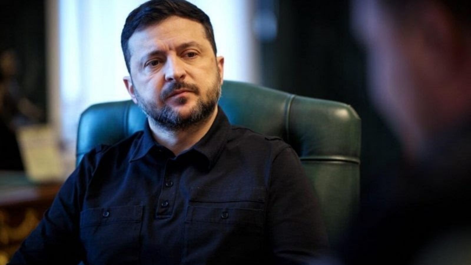Портрет президента України Володимира Зеленського, який сидить у кріслі під час інтерв'ю або офіційної зустрічі.