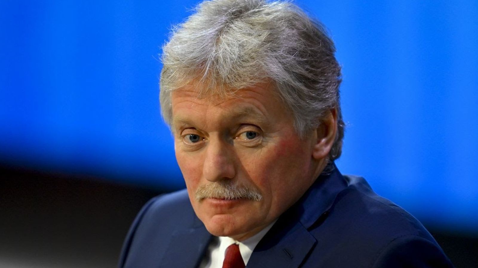 A portrait photo of Dmitry Peskov against a blurred blue background.