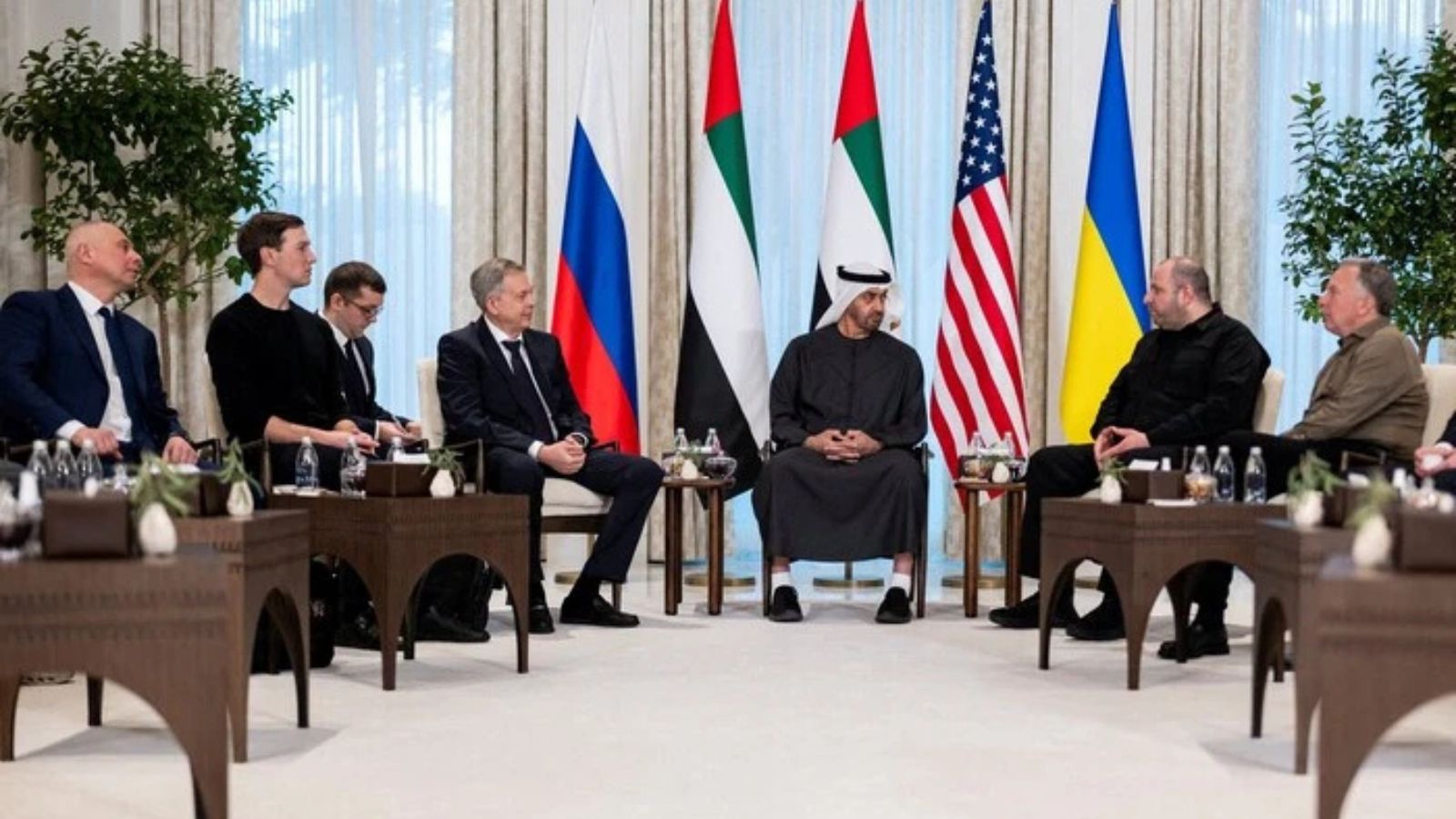 A wide shot of officials from the US, Russia, Ukraine, and the UAE sitting in a formal hall for trilateral peace negotiations.