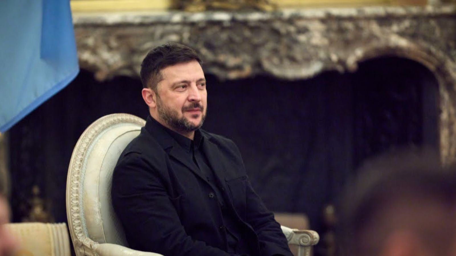 President of Ukraine Volodymyr Zelenskyy sits in a chair during an official meeting with a fireplace in the background.