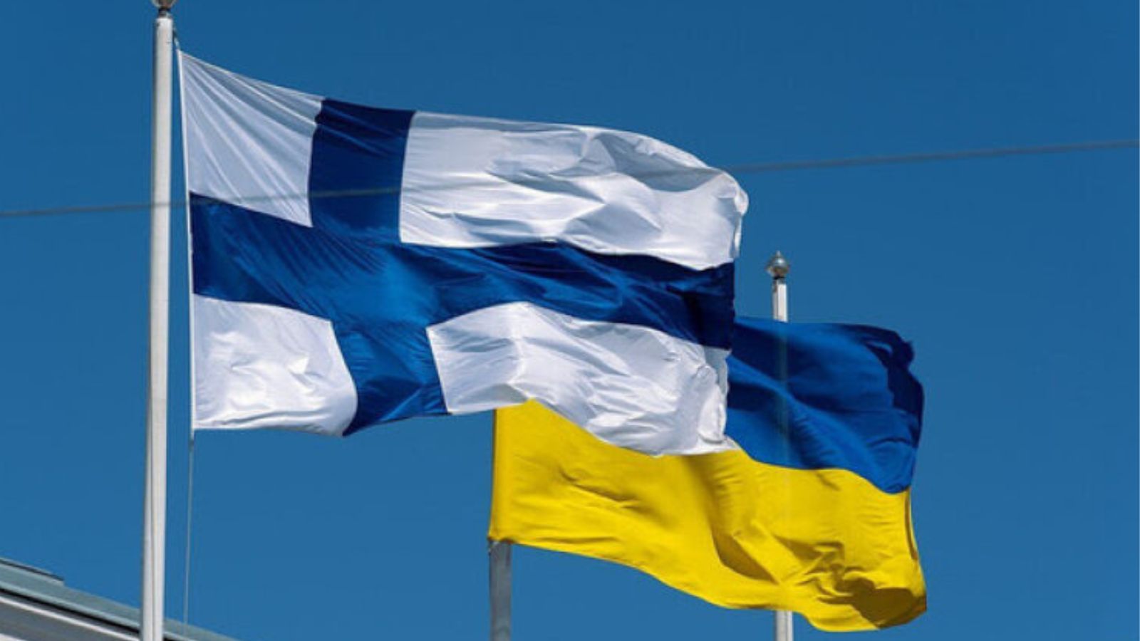 Flags of Finland and Ukraine waving side by side against a clear blue sky.
