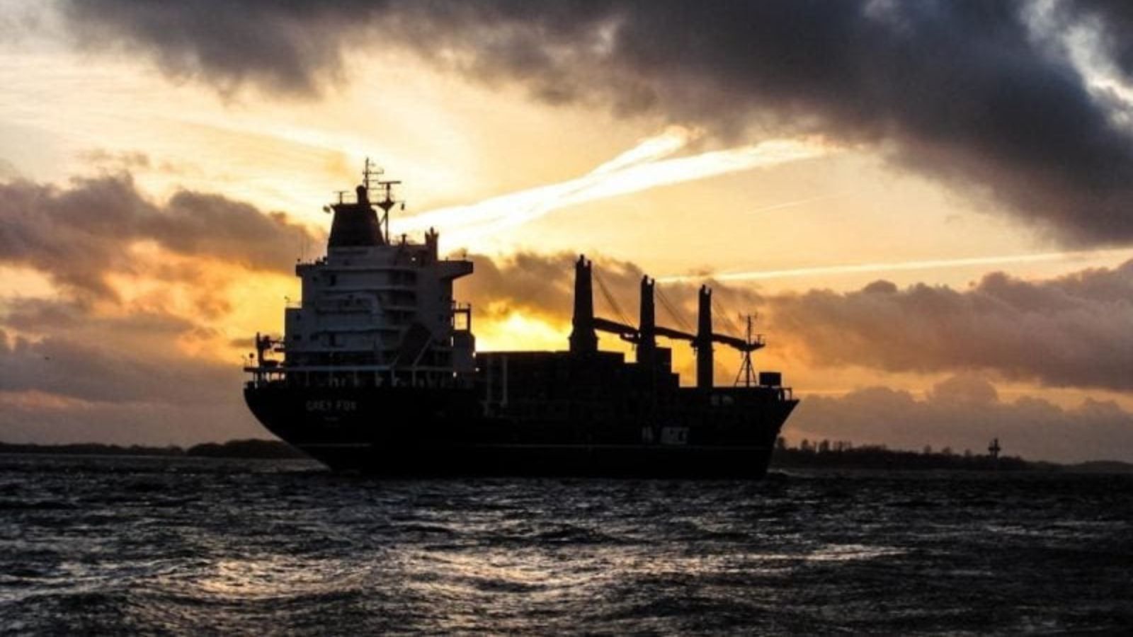 Silhouette of a large cargo ship at sea against an evening sky and sunset.