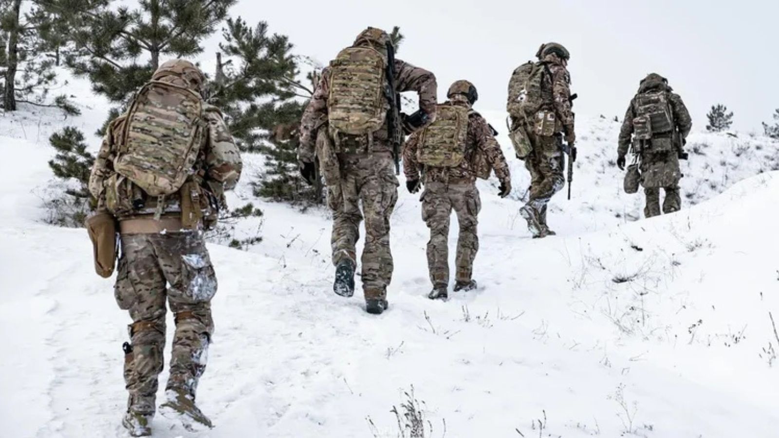 Five Ukrainian soldiers in full combat gear walking up a snow-covered hill while on a mission.