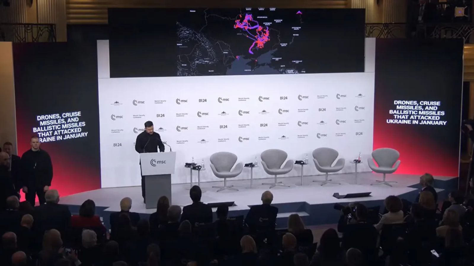Volodymyr Zelenskyy stands near a screen displaying a map of Ukraine with the trajectories of Russian missiles and drones.
