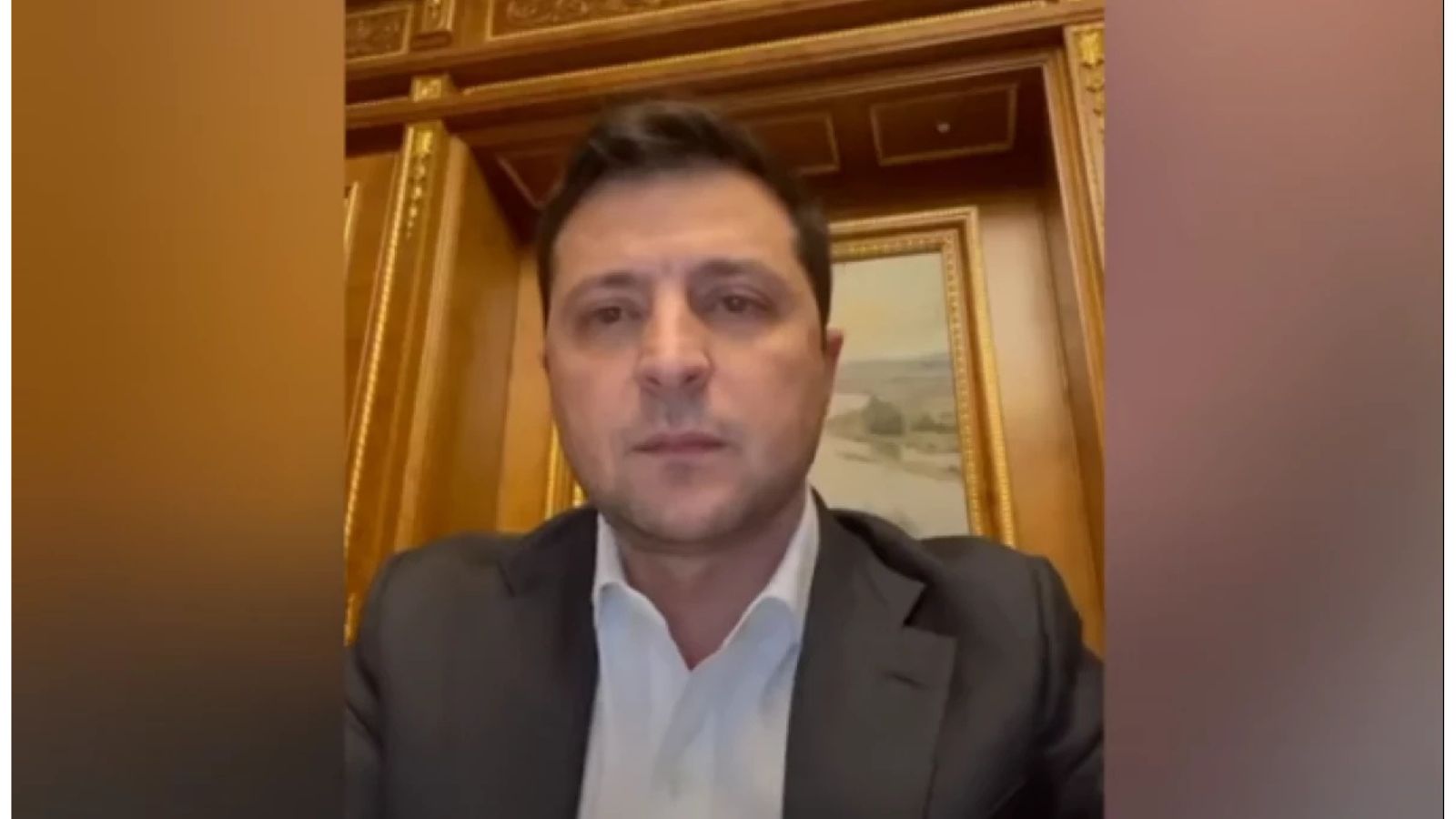 Screenshot of Volodymyr Zelenskyy's video address in a formal shirt and jacket against wooden panels on the first morning of the full-scale invasion.
