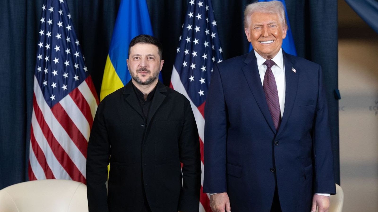 Official portrait of Volodymyr Zelenskyy and Donald Trump standing side by side in front of the flags of Ukraine and the United States.