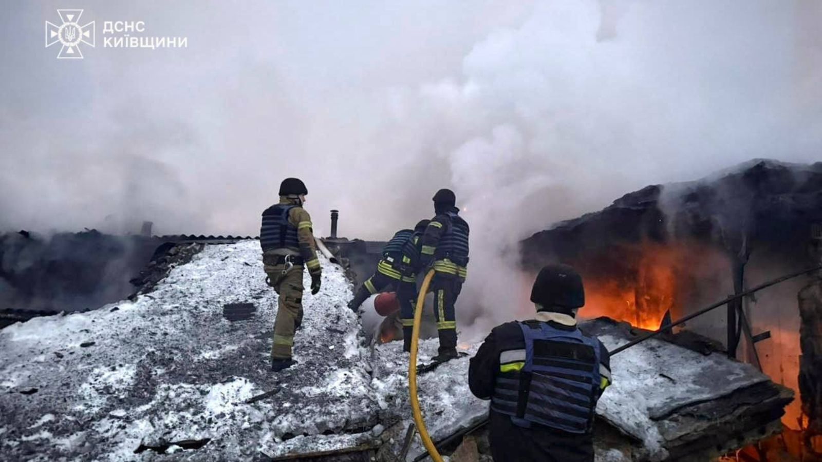 SES rescuers extinguishing a fire on the snow-covered roof of a building damaged by overnight shelling.