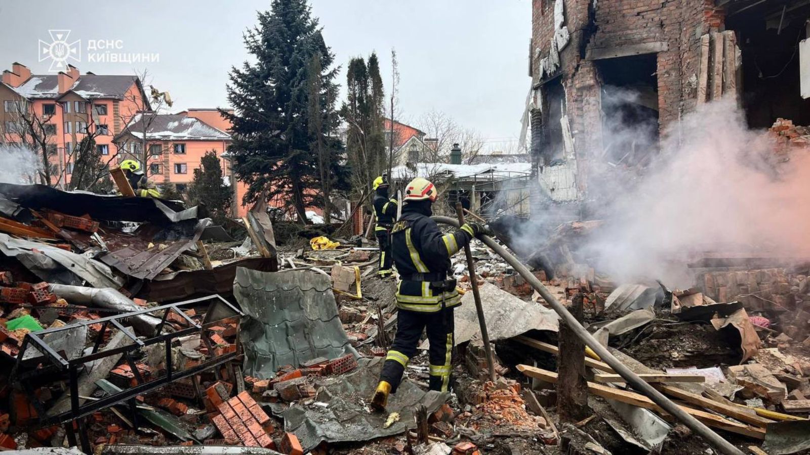 Firefighters working among the debris of a brick residential building partially destroyed by a missile strike.