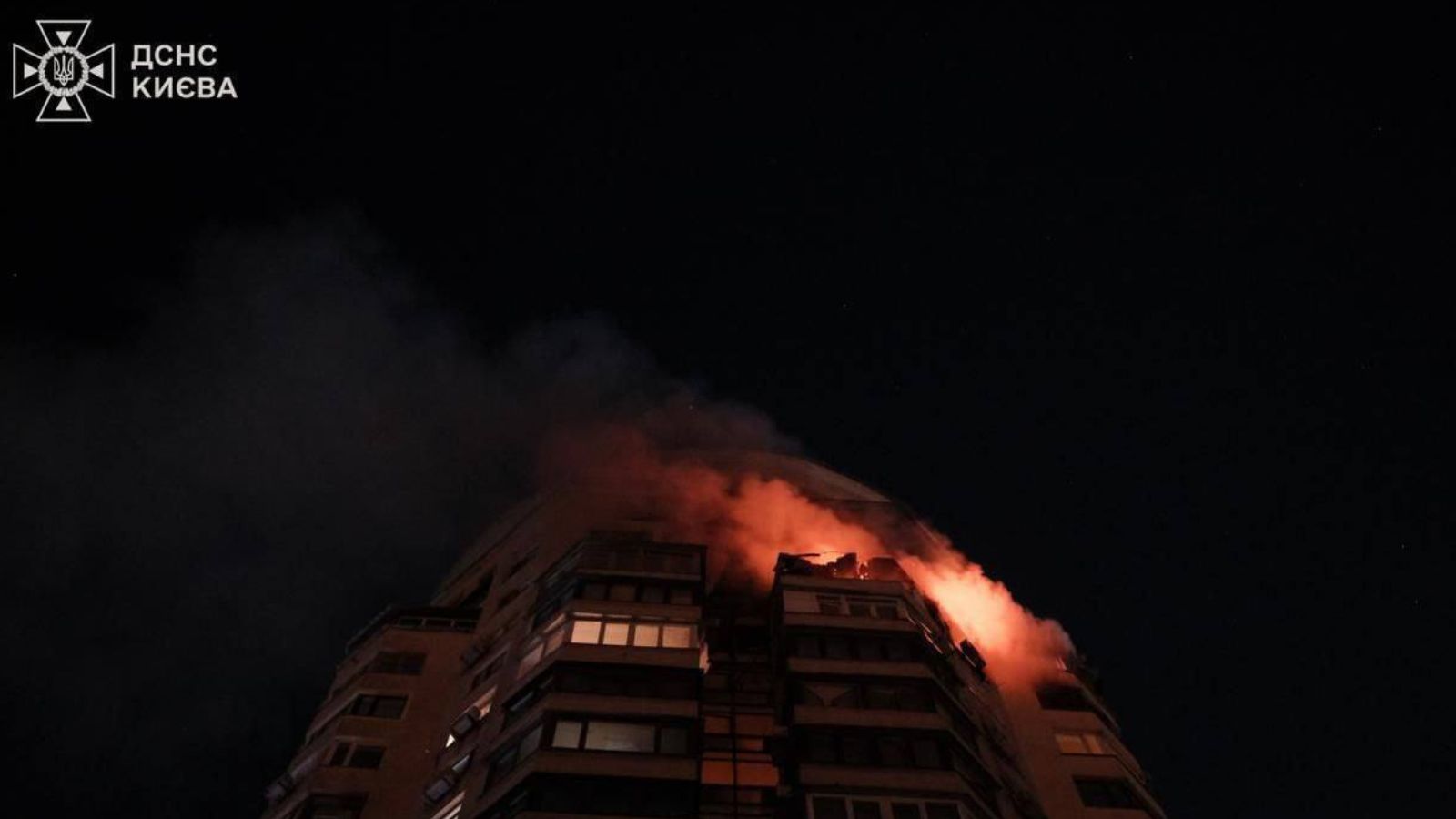 Upper floors of a residential high-rise building on fire and covered in smoke against the night sky.