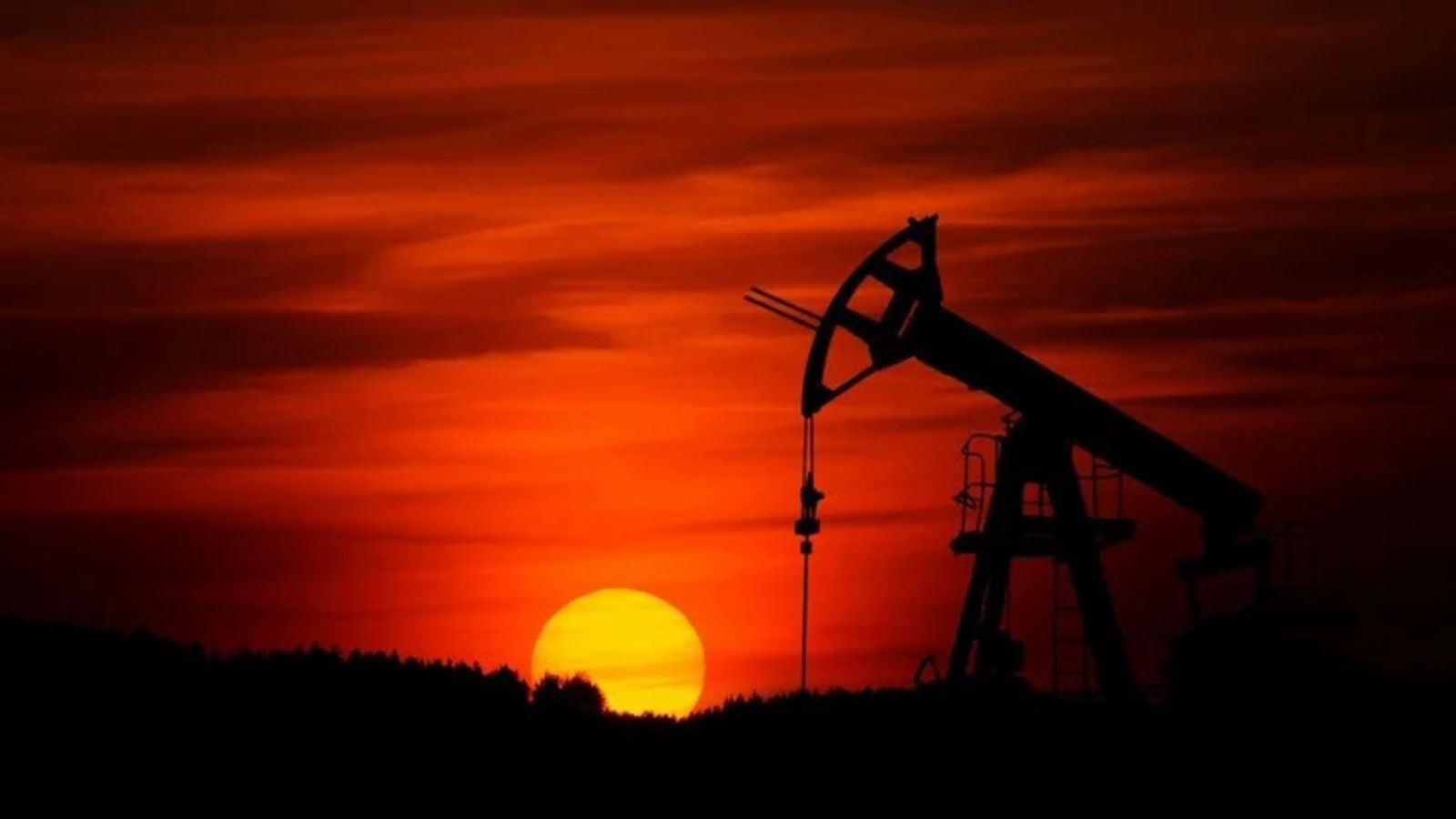 Silhouette of an oil pump jack against a bright orange sunset sky.