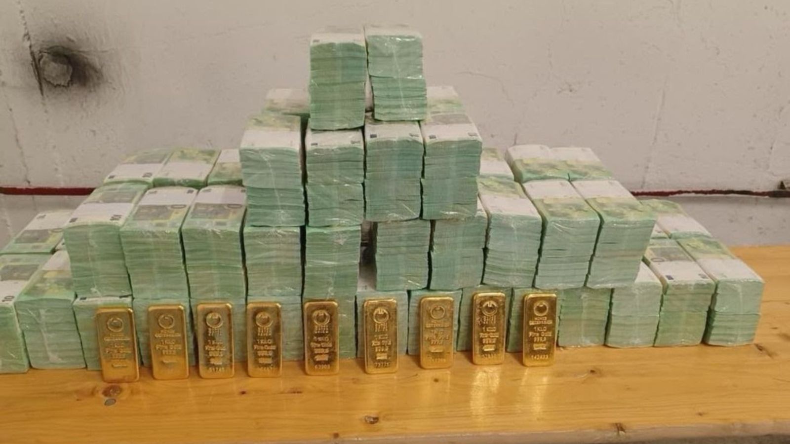 Вилучені пачки євро, складені пірамідою на столі, та ряд золотих злитків попереду них.