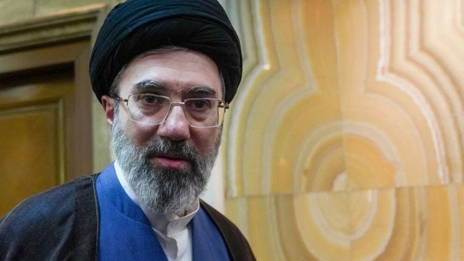 Portrait of Mojtaba Khamenei looking at the camera wearing glasses and a black turban.