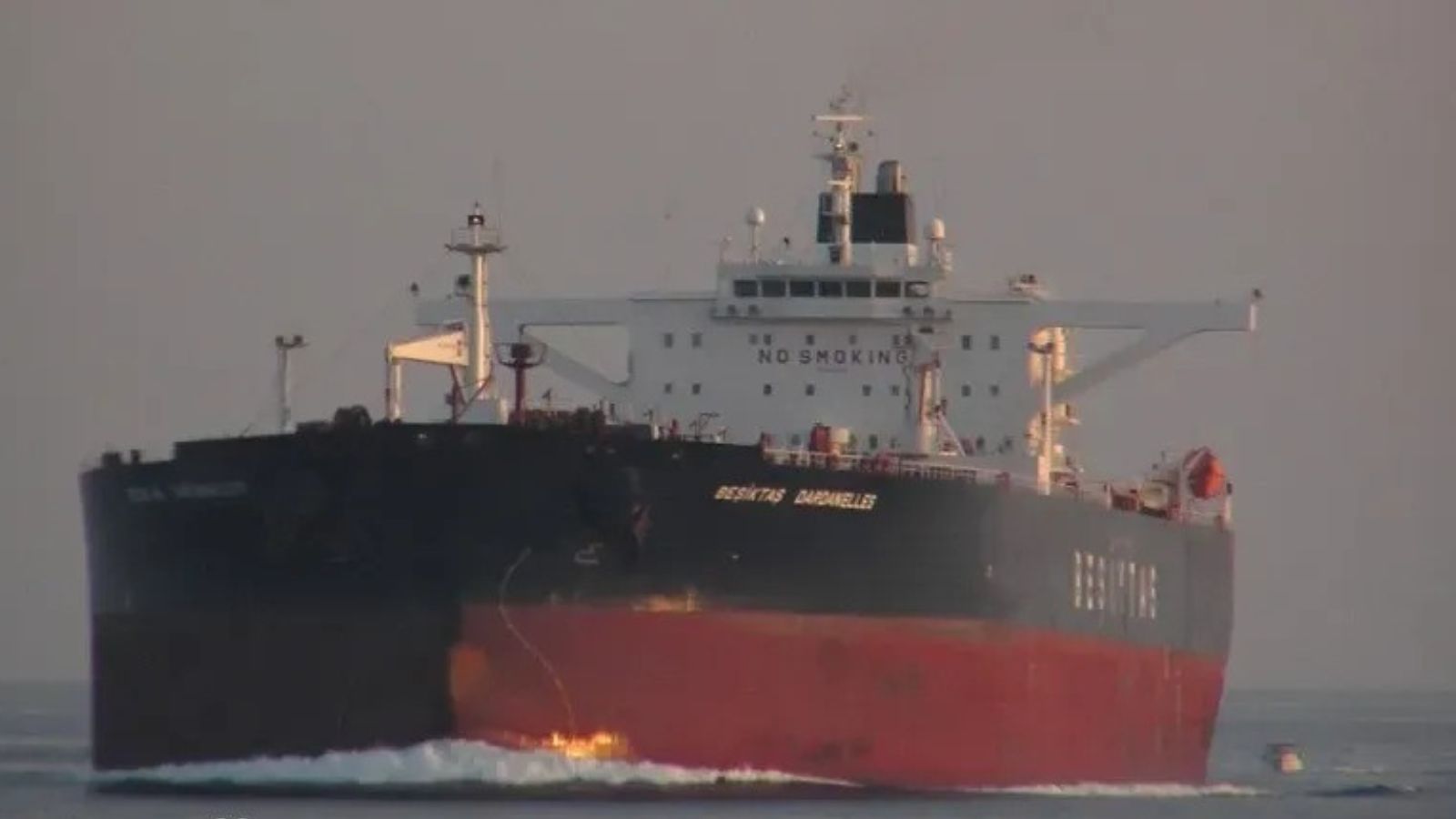 Close-up of the bow of a large oil tanker with the name "BESIKTAS DARDANELLES" on the hull, moving through water. White bridge superstructure and deck lighting are visible.
