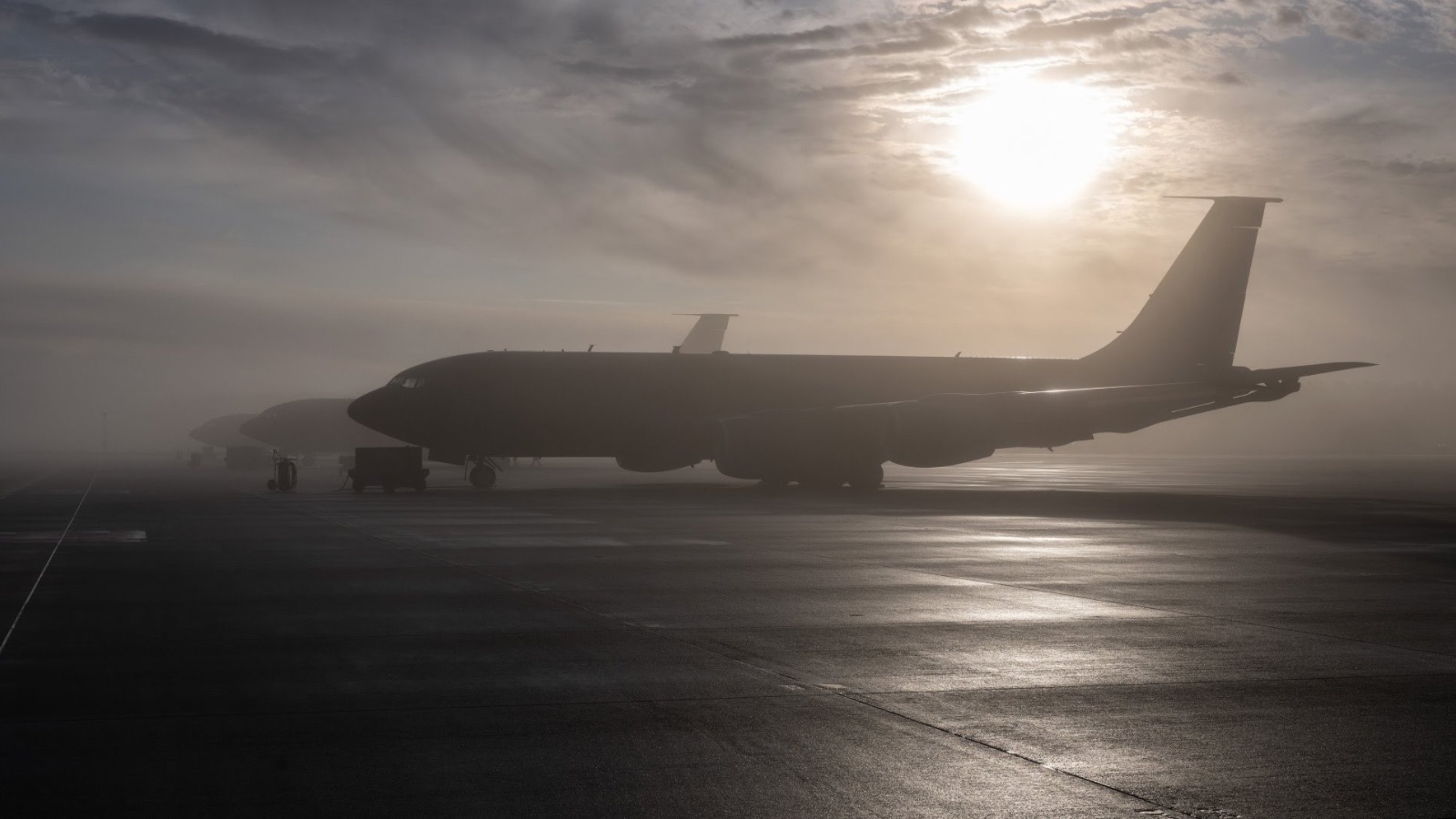 Silhouettes of Boeing KC-135 Stratotanker refueling aircraft on a runway at sunset during foggy weather.