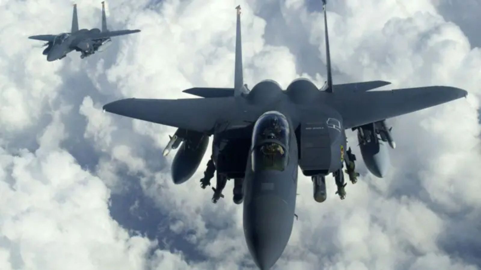 Two American F-15E Strike Eagle fighter jets flying above thick white clouds.