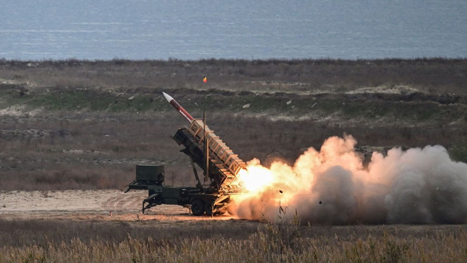 A mobile Patriot surface-to-air missile launcher firing a rocket in an open field.