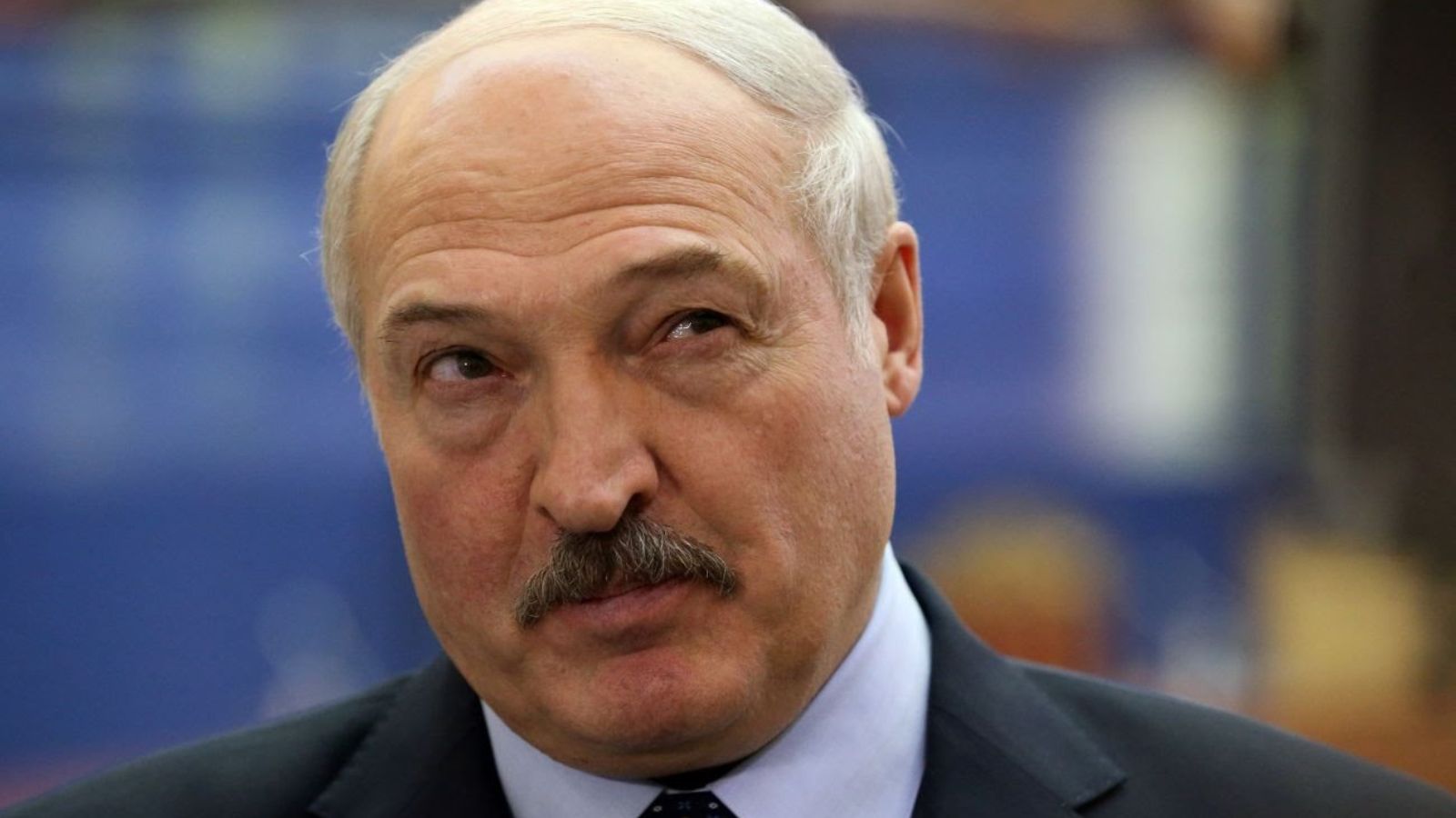 Close-up portrait of Alexander Lukashenko wearing a formal suit and tie against a blurred background.