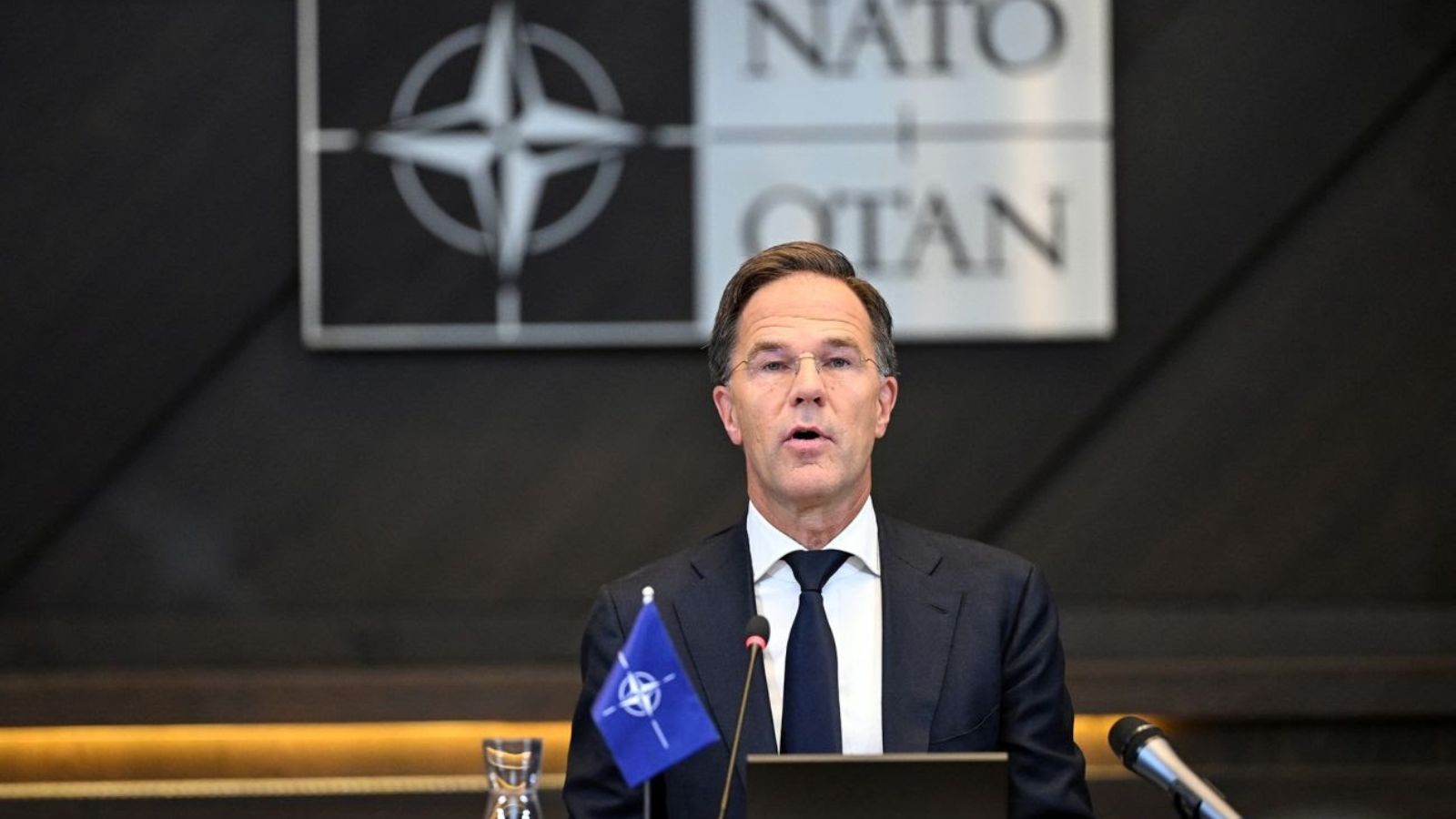 NATO Secretary General Mark Rutte during an official address against a dark background with the Alliance emblem.