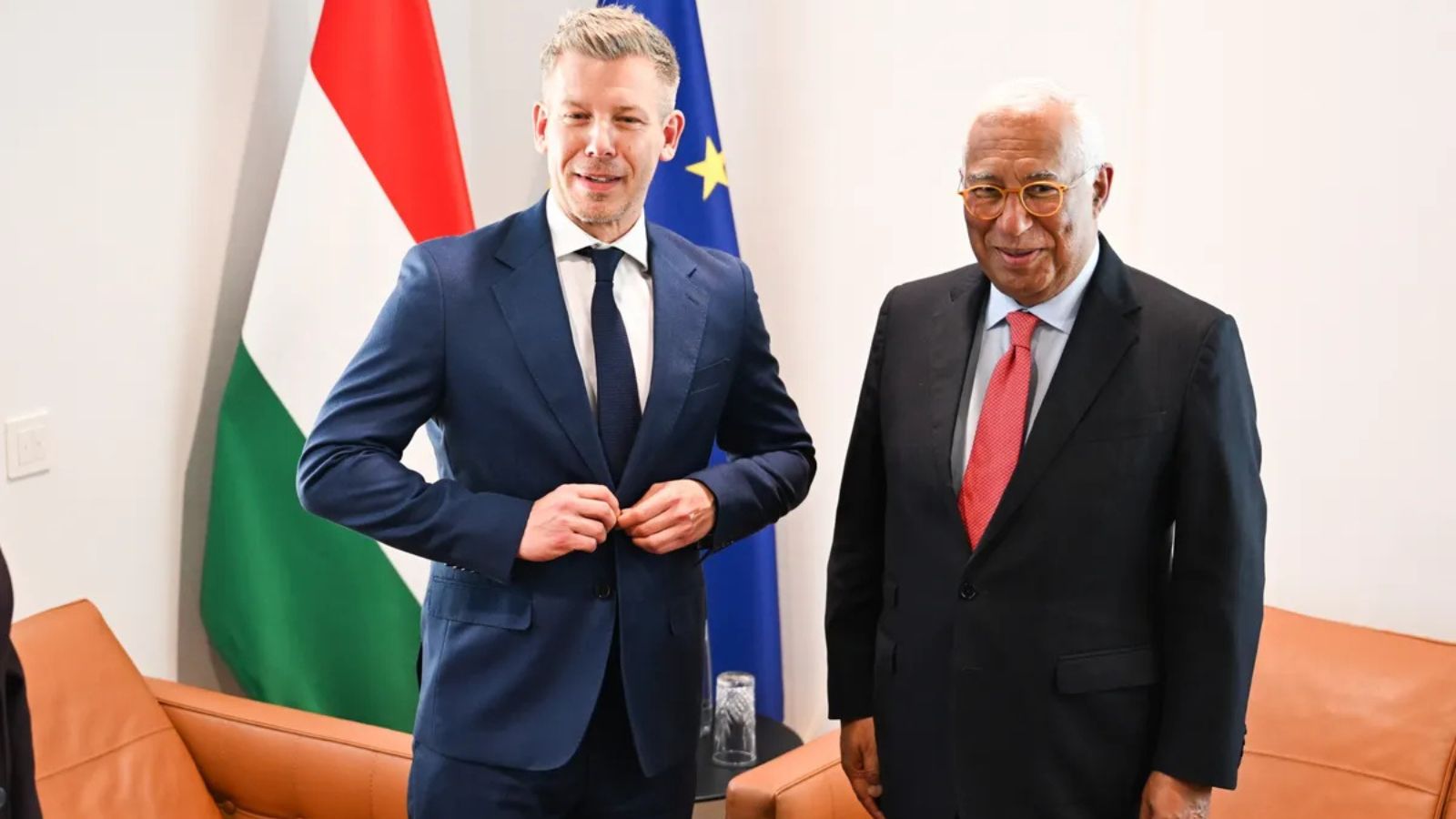 Peter Magyar and Antonio Costa standing together and smiling in front of the Hungarian and EU flags.