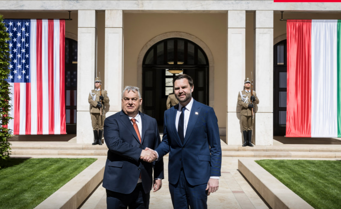 Орбан і Венс тиснуть одне одному руки надворі на фоні будівлі з прапорами Угорщини та США