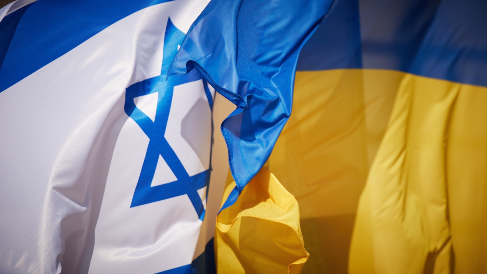 Державний прапор Ізраїлю та державний прапор України, що розвіваються поруч на сонячному фоні.