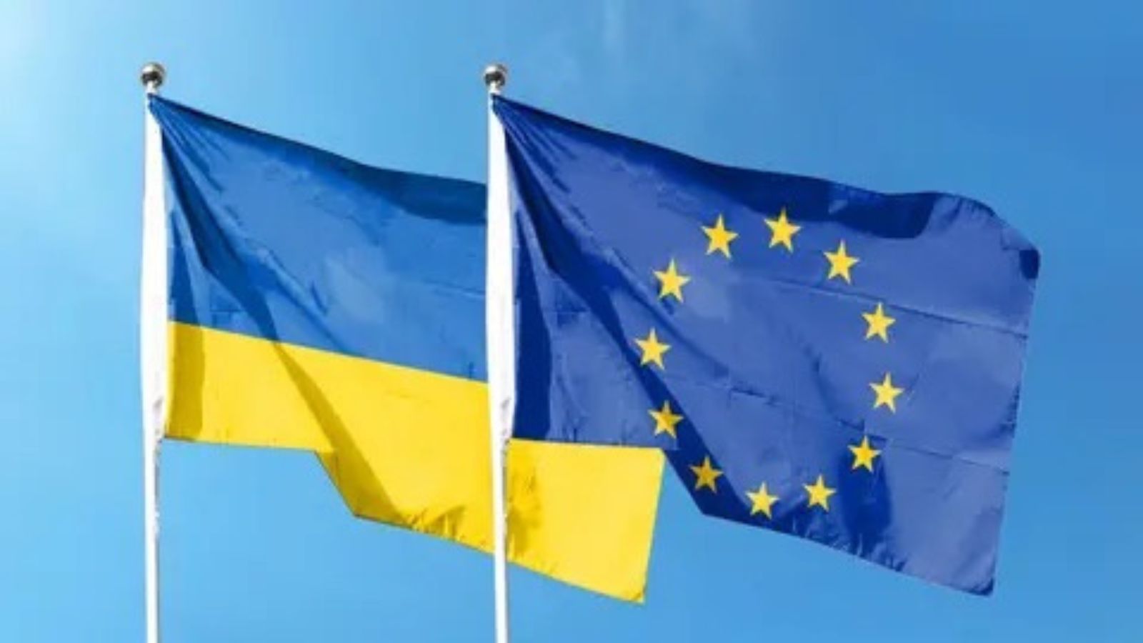 Прапори України та Європейського Союзу майорять поруч на флагштоках на фоні чистого блакитного неба.